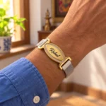 Personalized engraved name mesh bracelet with a golden oval nameplate, worn with a blue shirt