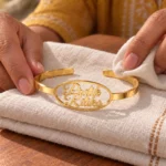 Gold-tone couple name bracelet with two script names inside an oval frame, displayed on folded cream fabric